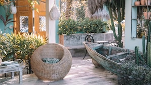 Une chaise en osier, une table en bois et la structure d’un bateau rustique, le tout dans un cadre de jardin.