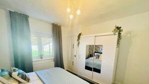 Un dormitorio con cama, armario, ventana con cortinas y una planta.