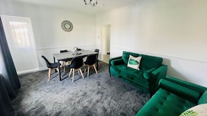 Una habitación con una mesa de comedor, seis sillas, un sofá verde y una araña.