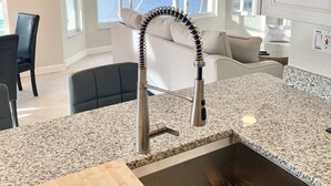Una cocina moderna con encimera de granito, pileta de acero inoxidable y vista a un puerto deportivo a través de amplias ventanas.