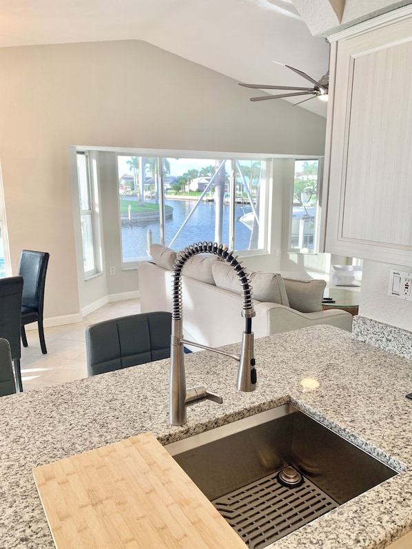 A modern kitchen with a granite countertop, stainless steel sink, and a view of a marina through large windows.