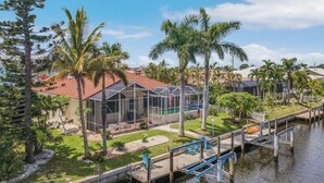 Una casa con piscina, rodeada de palmeras y un muelle que se adentra en el agua.