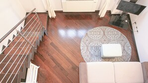 Ein modernes Wohnzimmer mit Holzboden, einem weißen Sofa, einem gemusterten Teppich und einer Treppe mit Metallgeländern.