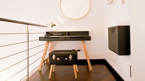 Ein modernes Zimmer mit Schreibtisch, rundem Spiegel, Fernseher und Koffer.