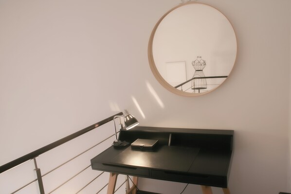 A modern desk with a laptop and a lamp, a round mirror on the wall, and a staircase railing. - BnButler - Bergonzoli 3 (Milan)