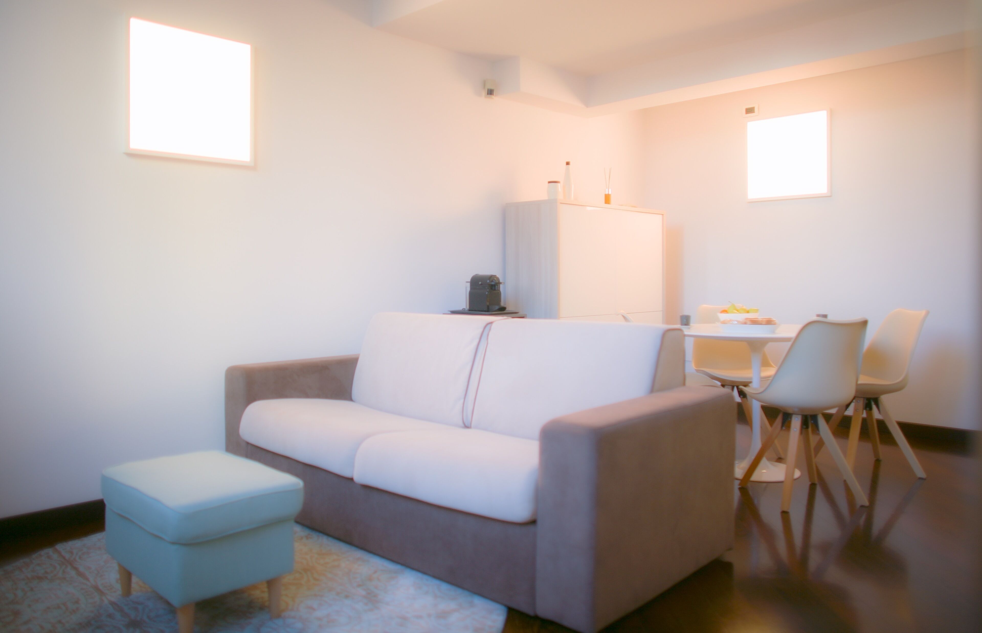 Un salon moderne comprenant un canapé, un petit pouf, une table basse et un coin repas avec des chaises.
