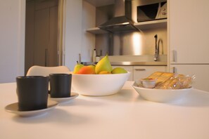 A kitchen with a white countertop, a bowl of fruit, two black cups, and a plate with bread. - BnButler - Bergonzoli 3 (Milan)