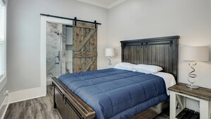 A bedroom with a bed, a wooden headboard, a nightstand, a lamp, a ceiling fan, and a sliding door with a wooden panel.