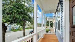 A covered porch with a wooden floor, white railings, and a view of a residential street.