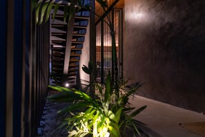 A narrow pathway leading to a staircase with a metal railing, surrounded by greenery.