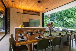 A modern dining area with a long wooden table set for multiple guests, surrounded by green chairs.