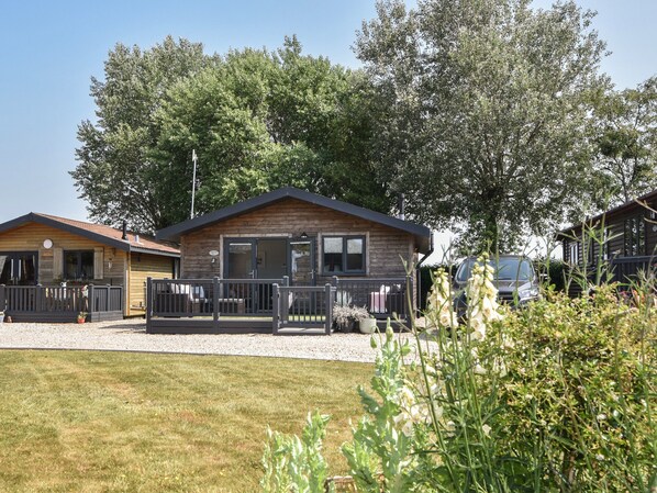 A wooden cabin with a porch, surrounded by trees and a gravel driveway. - Oakwood 2 @ Pinewood Retreat (Axminster)