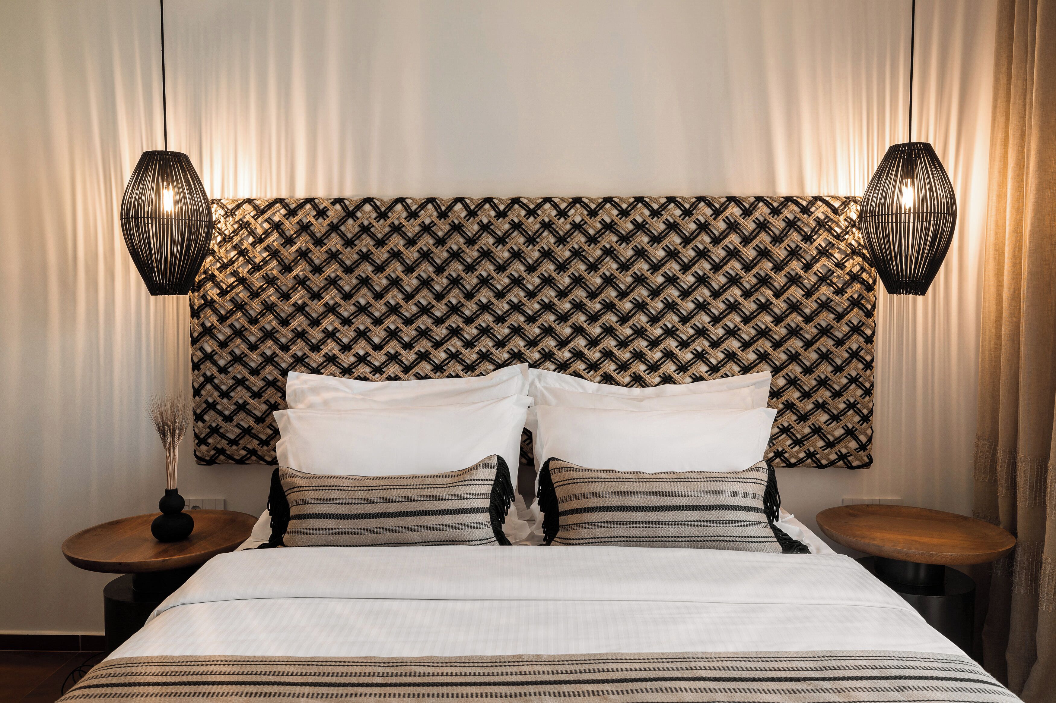 A neatly made bed with white and striped bedding, two bedside tables with lamps, and a patterned headboard.