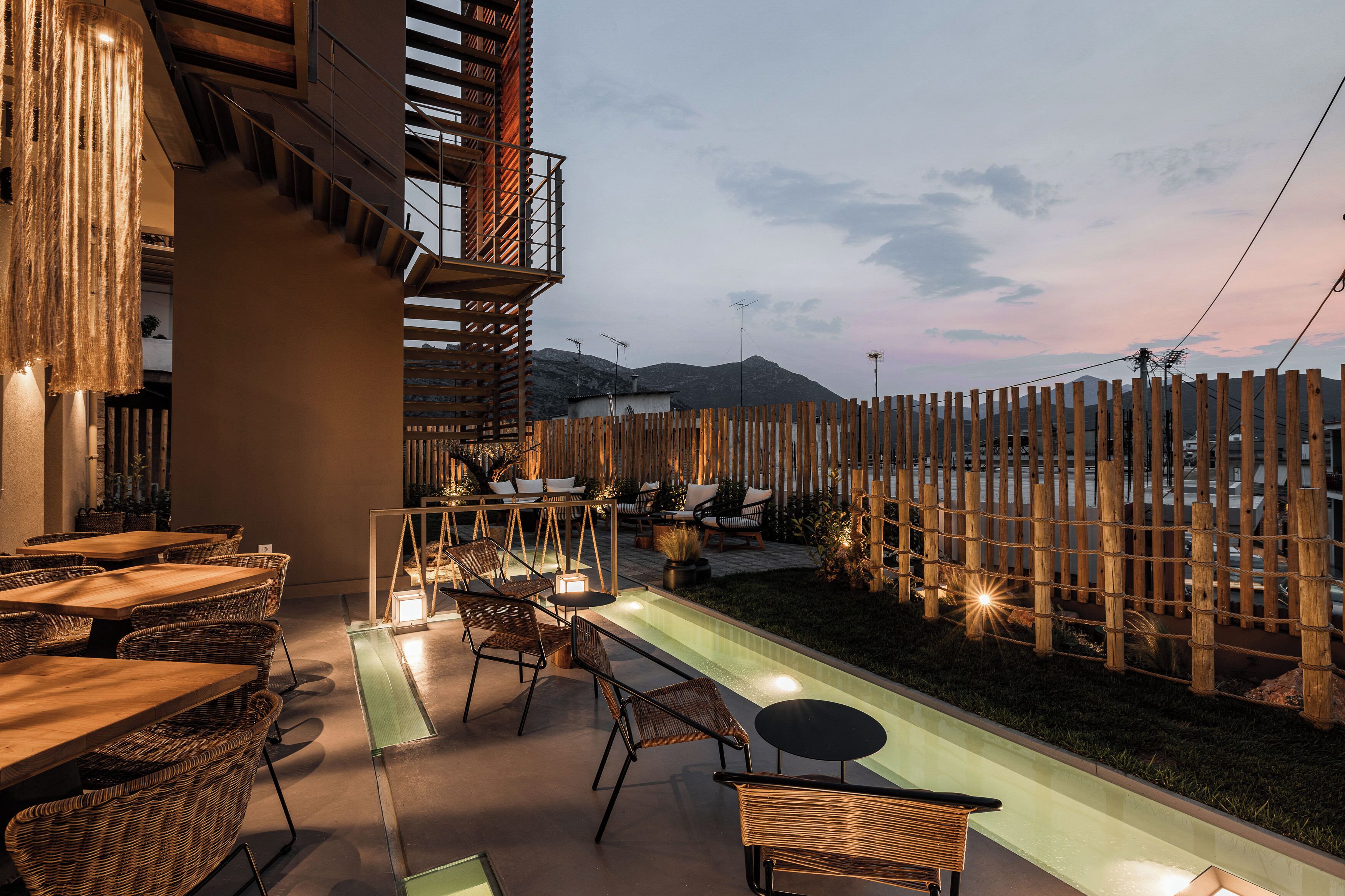 An outdoor dining area with wicker furniture and a pool, surrounded by a wooden fence and mountains in the background.