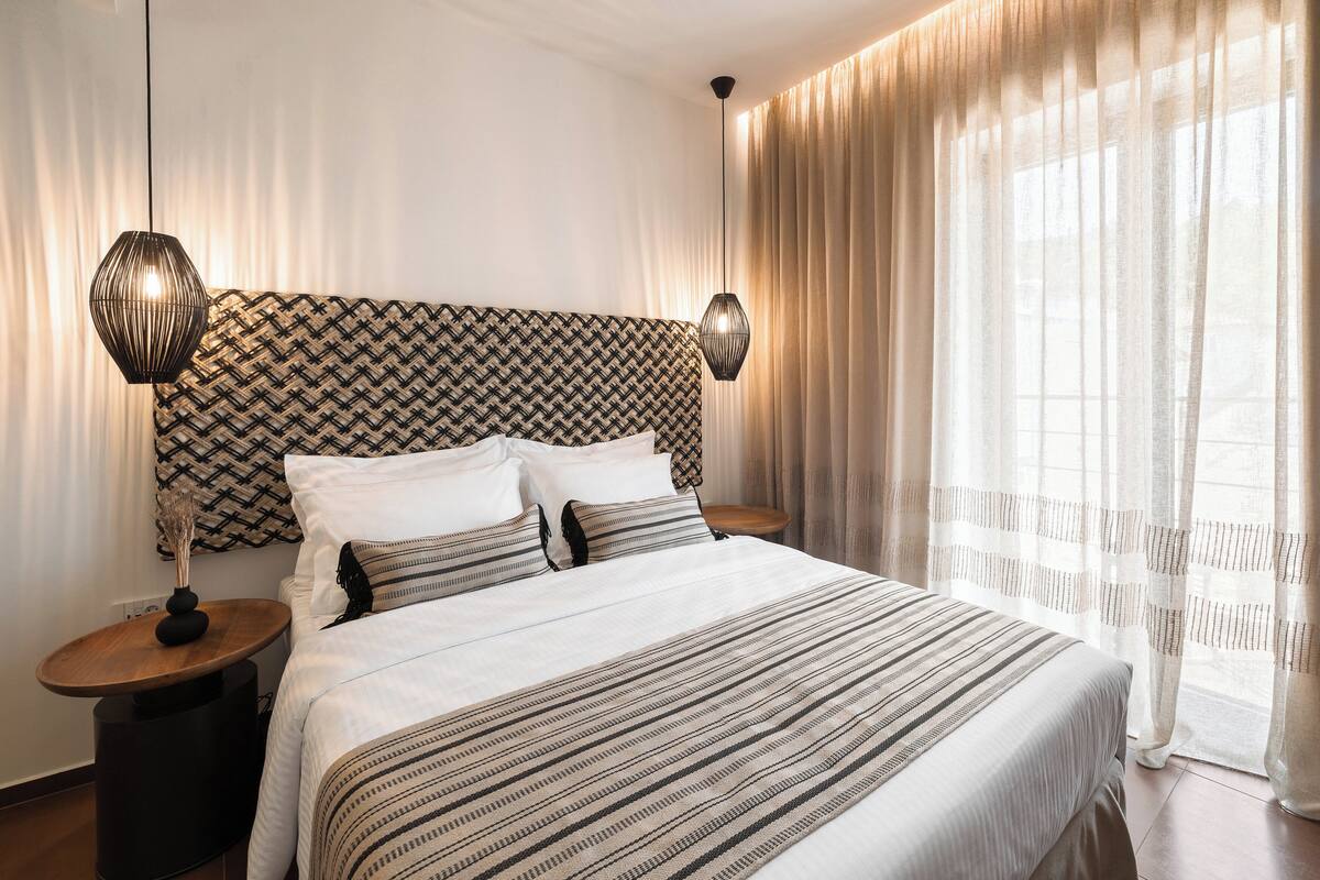 Una cama bien hecha con ropa de cama a rayas, un cabecero estampado y dos lámparas de noche.