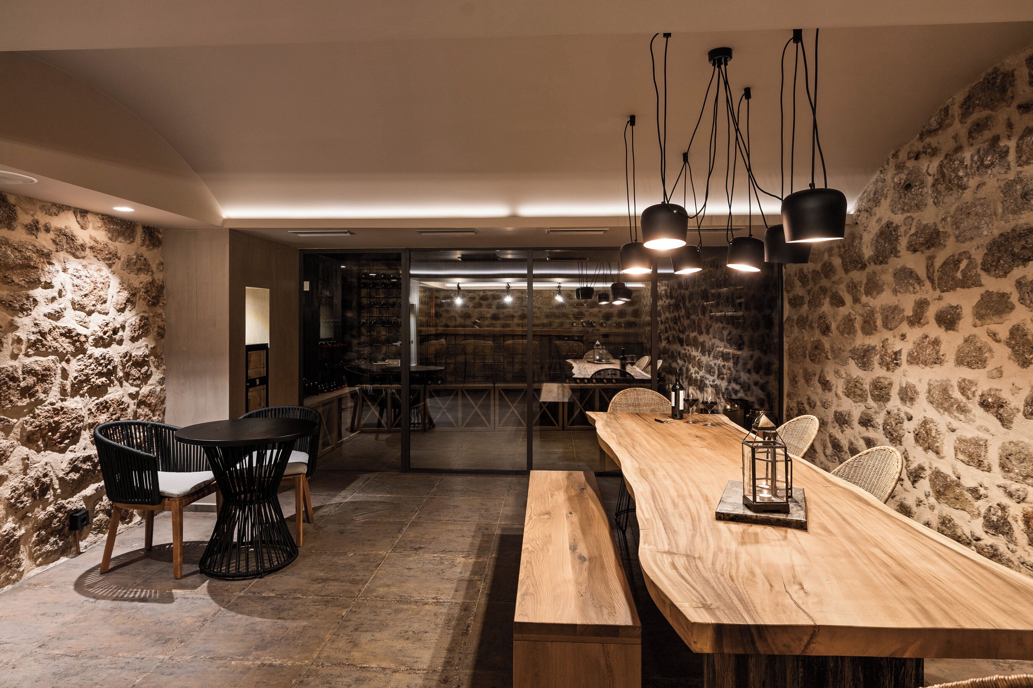 Un interior rústico con una mesa y sillas de madera, paredes de piedra y lámparas colgantes.