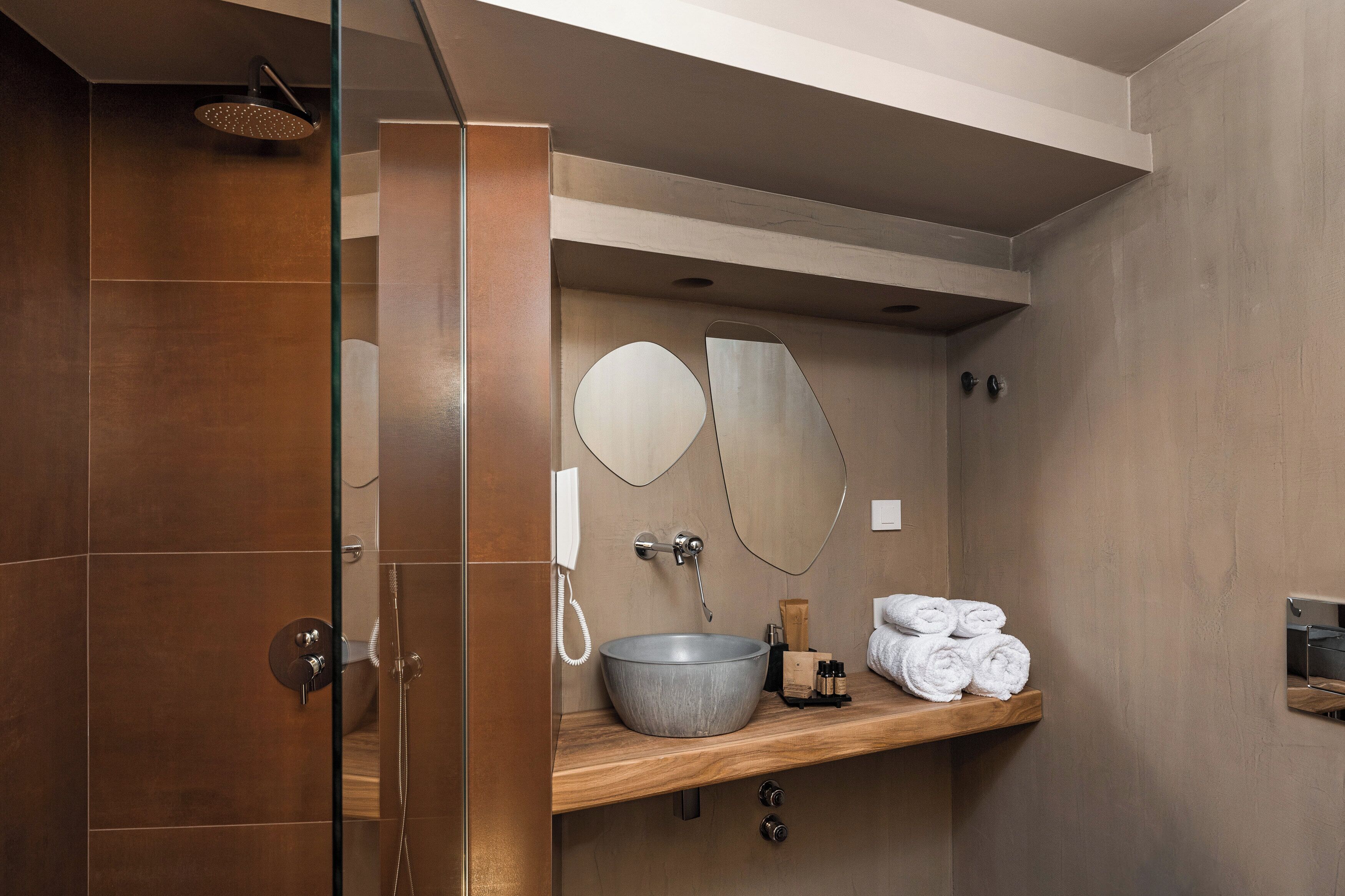 A modern bathroom with a wooden vanity, a large mirror, a round sink, and neatly folded towels on a shelf.