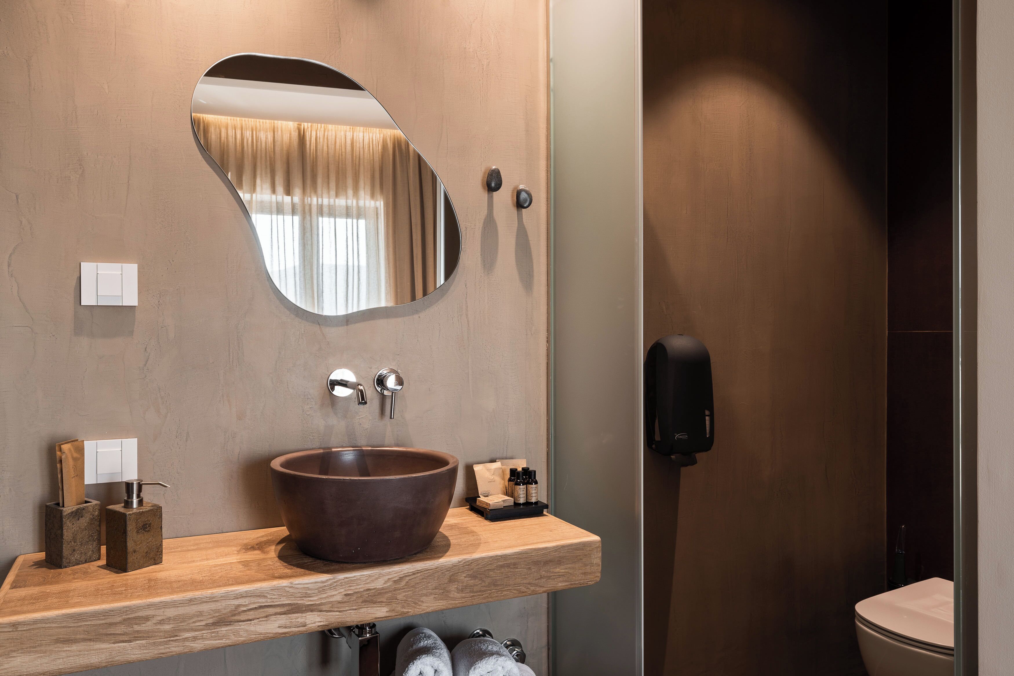 Une salle de bain moderne avec un meuble-lavabo en bois, un grand miroir, un lavabo sur colonne et une douchette à main.