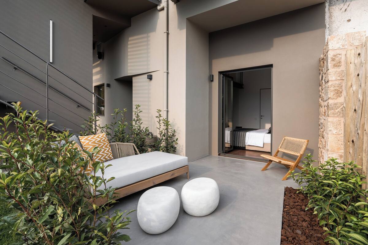 Un espacio exterior moderno con un sofá, dos taburetes redondos y una silla de madera.