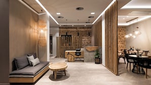 A modern interior with a sofa, round wooden table, stone wall, and a dining area with chairs and a table. - Kera Neme (Nemea)