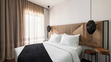 Une chambre d’hôtel avec un grand lit, une tête de lit en bois, deux lampes suspendues et un petit tabouret en bois.