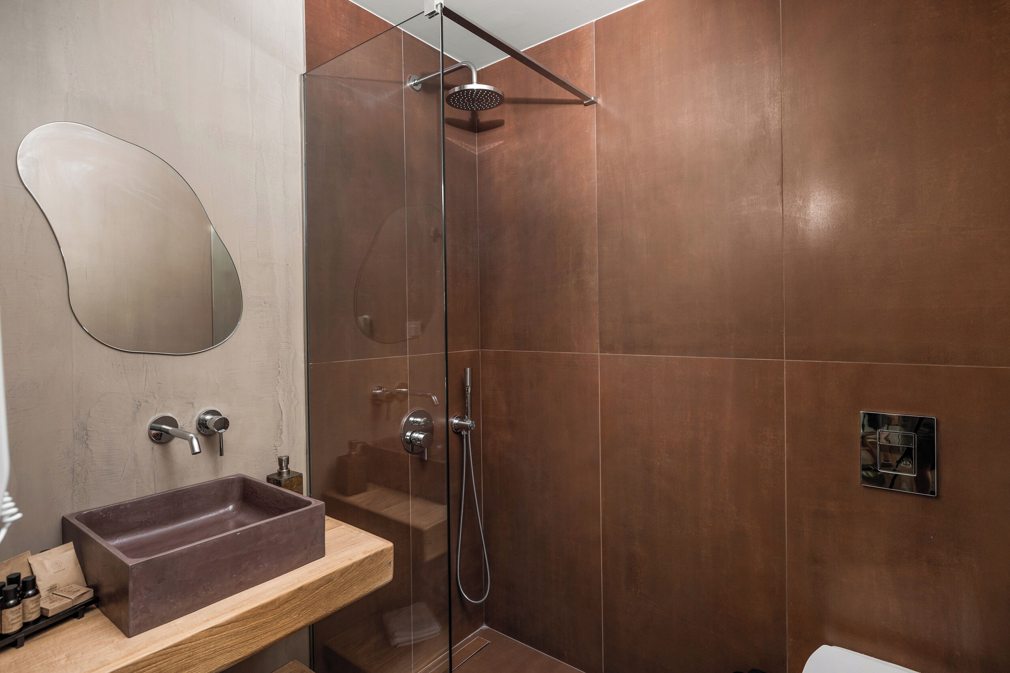 Un baño moderno con ducha envuelta en vidrio, tocador de madera con lavamanos marrón y un espejo grande.