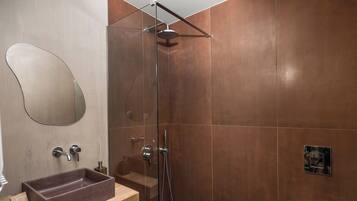 Un baño moderno con ducha envuelta en vidrio, tocador de madera con lavamanos marrón y un espejo grande.