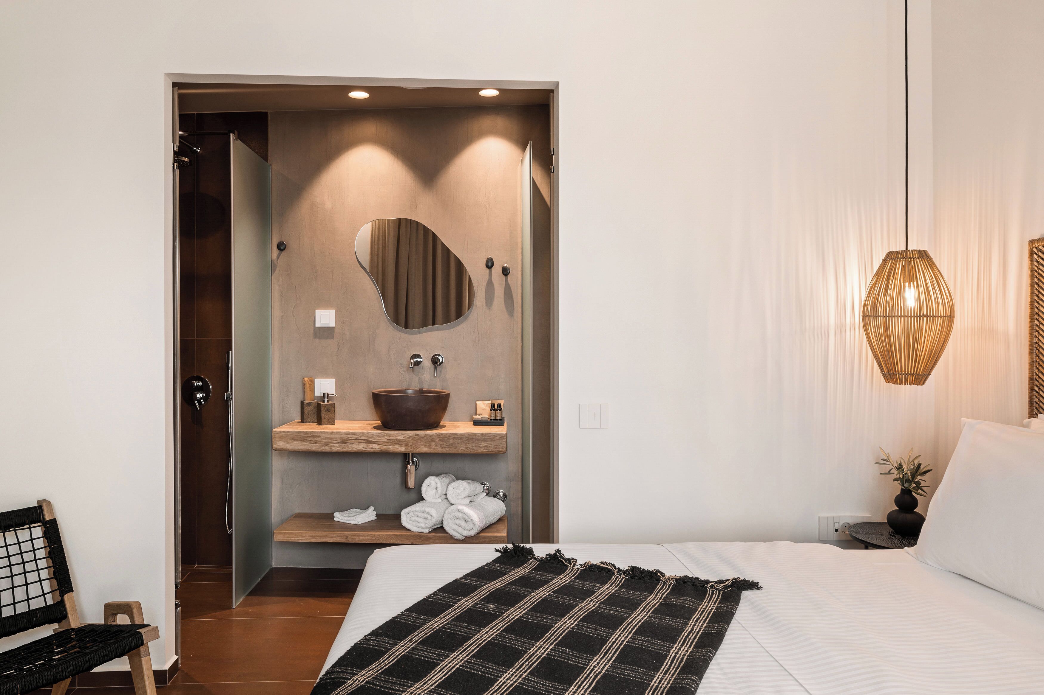 Een moderne hotelkamer met een groot bed, een houten kaptafel met spiegel, een rond wastafel en een klein rond tafeltje met een plantje.