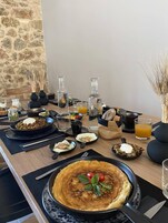 Un desayuno con diversos platos, como panqueques, huevos y tostadas, sobre una mesa de madera con una pared de piedra al fondo.