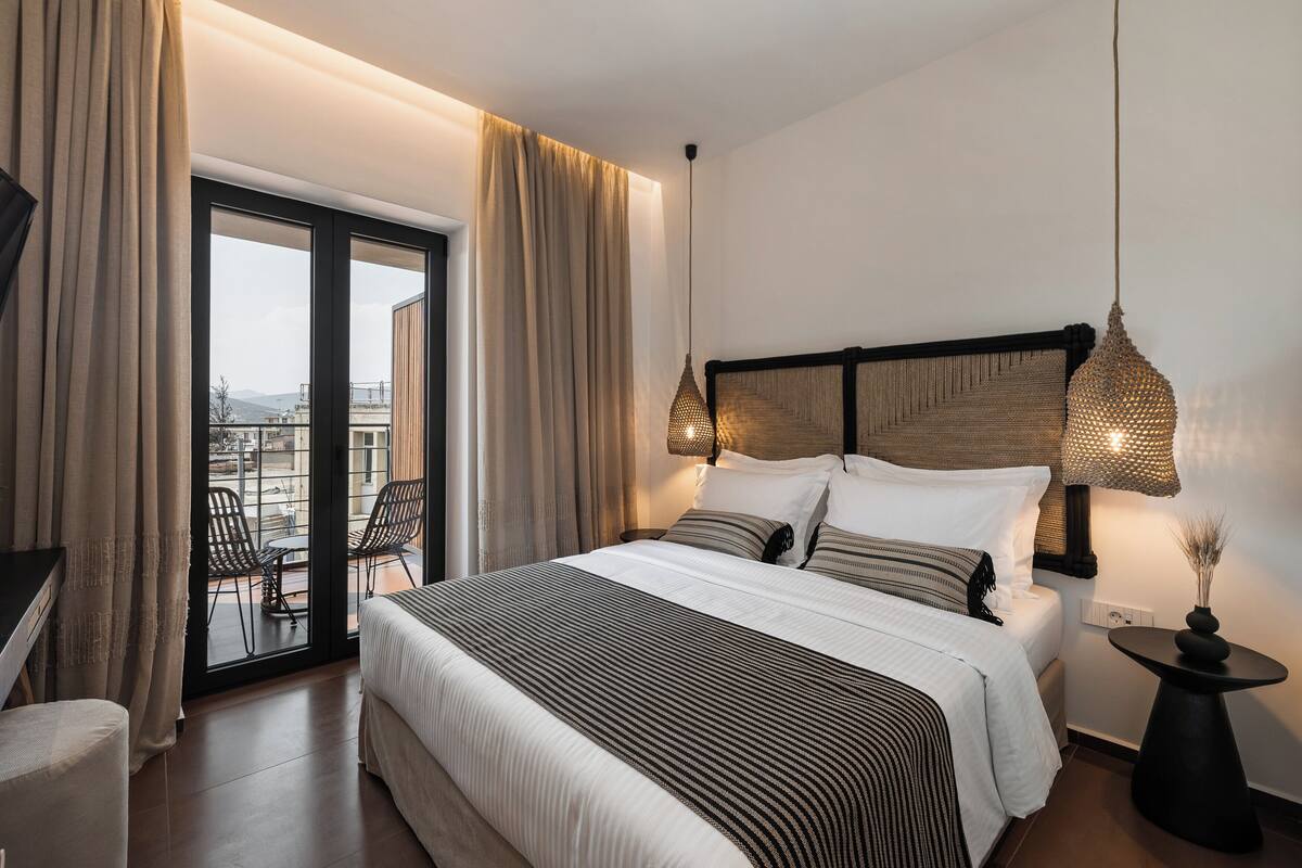 Una habitación de hotel con una cama grande, un balcón con sillas y vistas a la ciudad.