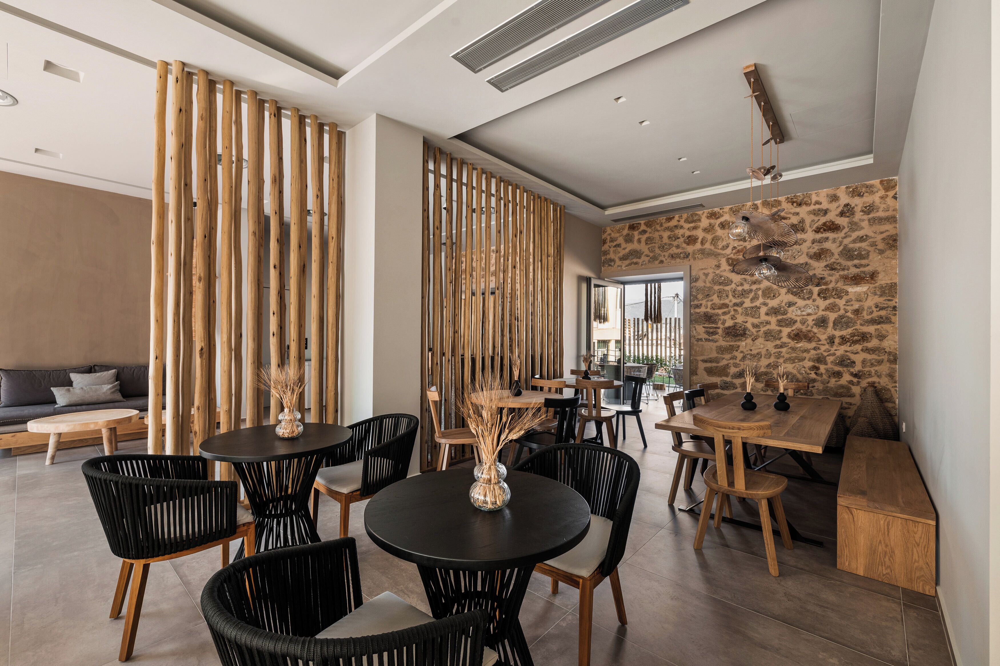 A modern dining area with round tables, black chairs, and a stone wall.
