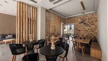 A modern dining area with round tables, black chairs, and a stone wall.