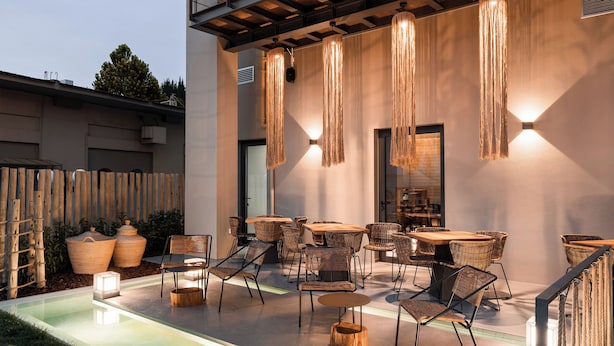 An outdoor patio area with wicker furniture, hanging light fixtures, and a pool. - Kera Neme (Nemea)