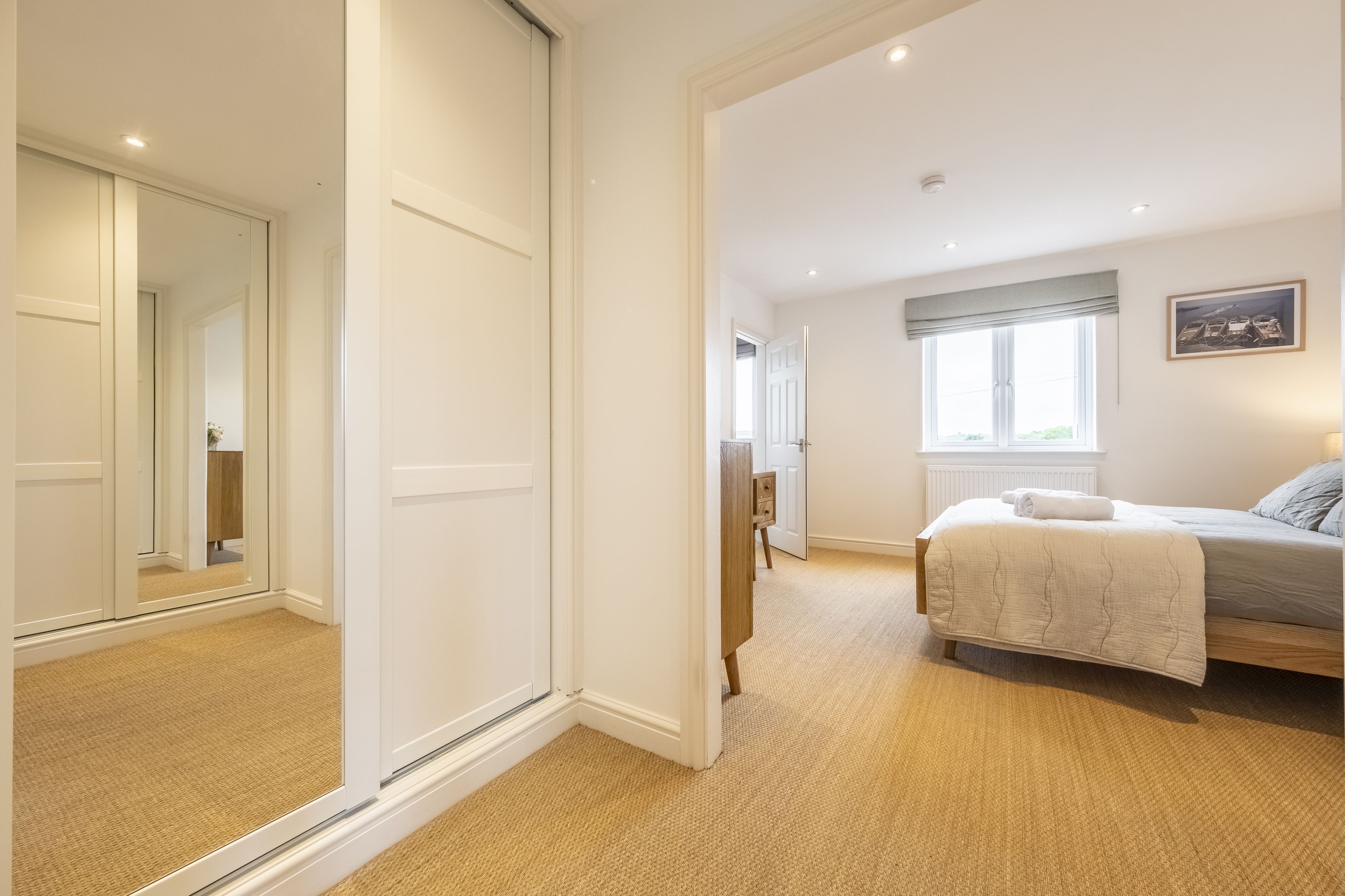 A bedroom with a bed, a nightstand, a window, and a door leading to another room.