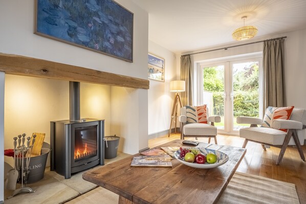 A cozy living room with a wood-burning stove, a comfortable sofa, and a dining table with a bowl of fruit.