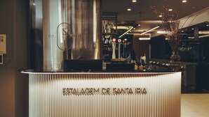 Una recepción con diseño moderno, una gran estructura metálica al fondo y una elegante lámpara colgante arriba.