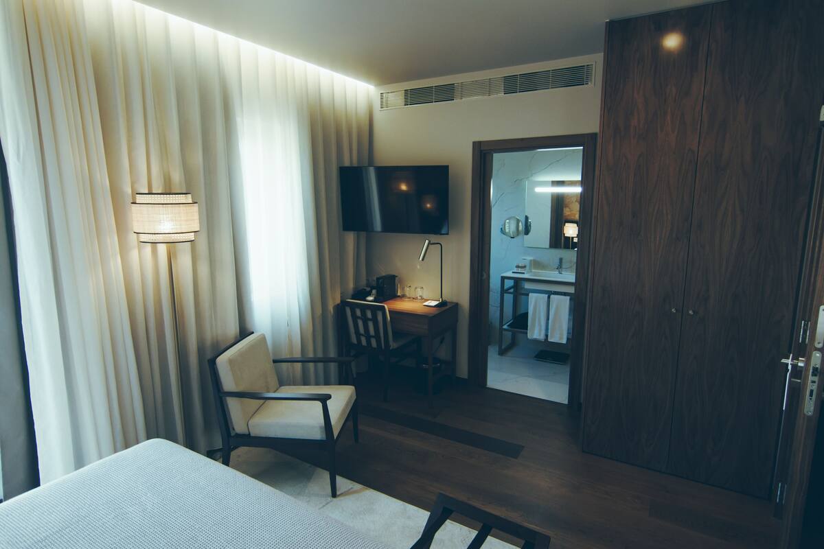 Una habitación de hotel con cama, escritorio, silla, televisor y armario de madera.