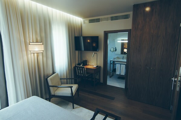 Una habitación de hotel con cama, escritorio, silla, televisor y armario de madera.