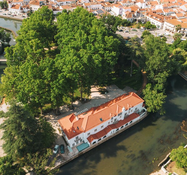 A riverside building with a red-tiled roof, surrounded by lush green trees.