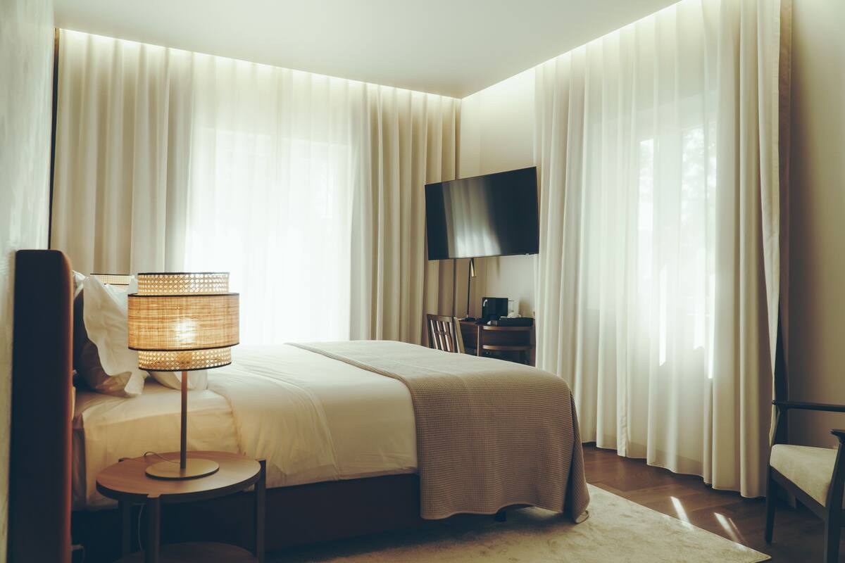 Una habitación de hotel con cama, televisión, lámpara y cortinas.
