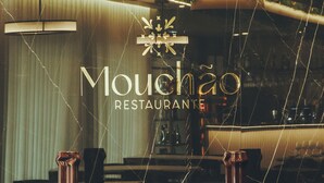 Interior de restaurante con diseño moderno, destacando una barra de mármol negro, estantes de madera con platos y copas, y una pared decorativa con plantas.