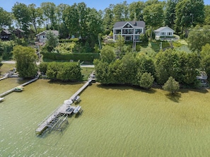 A large house surrounded by dense greenery and a dock extending into a calm body of water. - Luxury Lake Home with Private Dock (Petoskey)