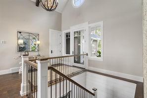 A spacious interior with a wooden staircase, white walls, and a large window providing a view of the outside. - Luxury Lake Home with Private Dock (Petoskey)