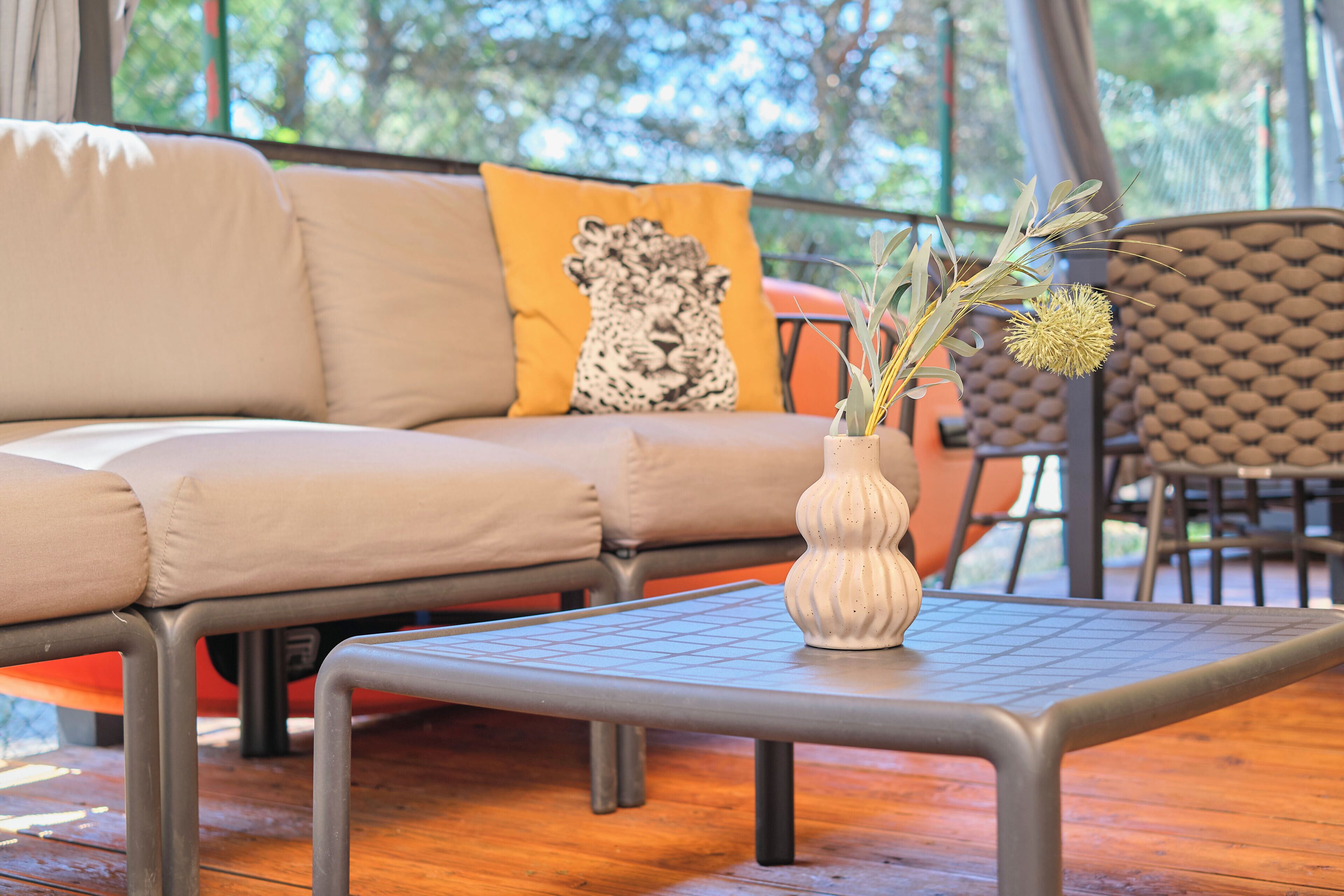 Un salón moderno con un sofá, un cojín estampado, una mesita y un jarrón con plantas secas.