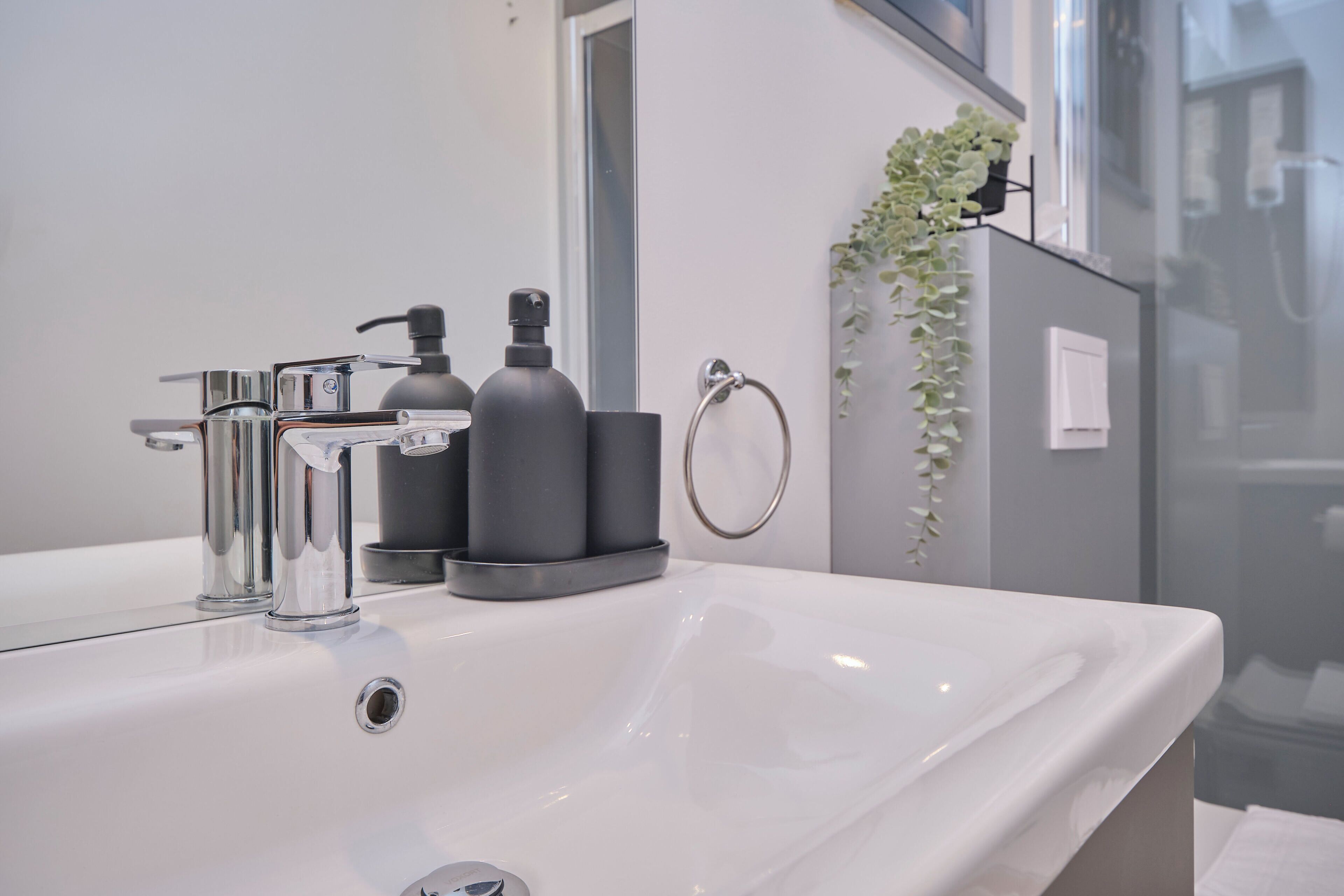 Casa de banho moderna com lavatório branco, torneira cromada, dispensador de sabonete preto e frasco de vidro para sabonete.