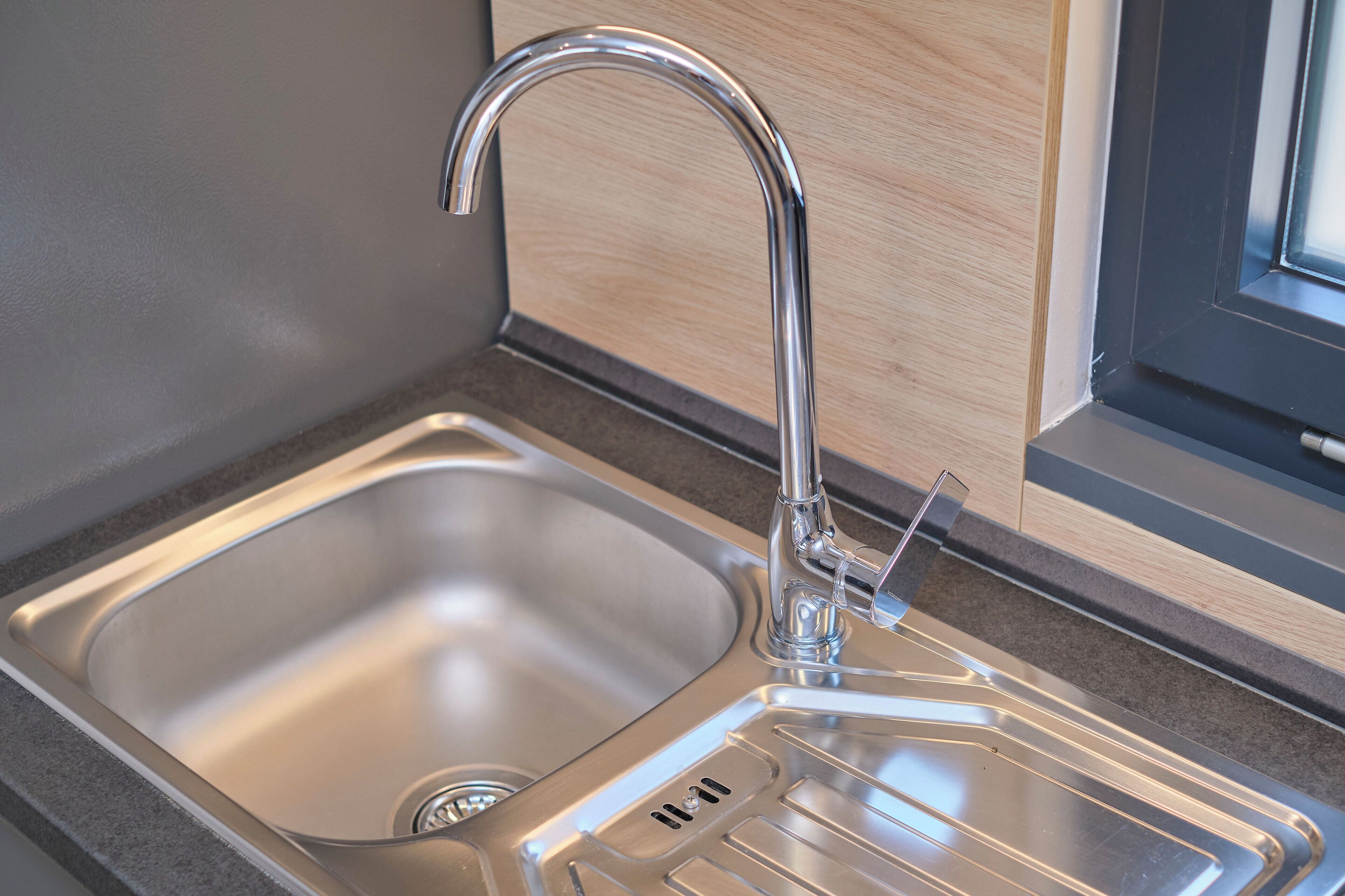 Eine moderne Küche mit Spüle aus Edelstahl, einem Wasserhahn und einem Fenster.