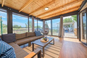 Ein modernes Interieur mit Holzboden, großen Fenstern, einer Couch, einem Couchtisch und einem Balkon mit Aussicht.