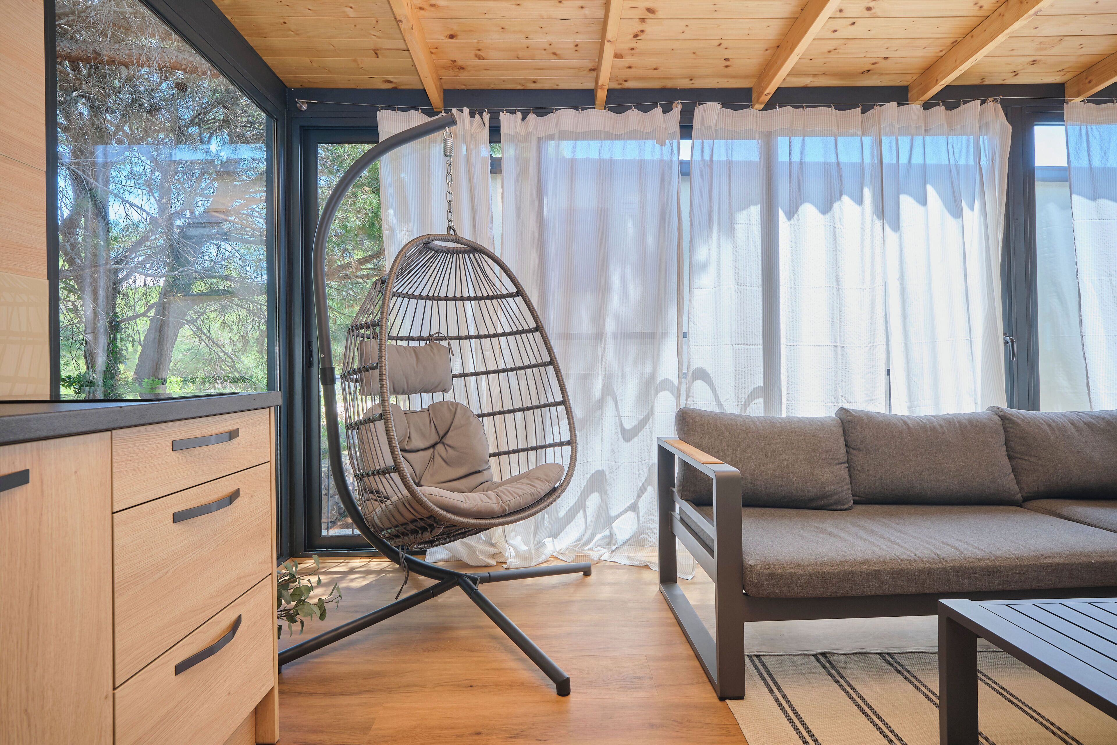 Una habitación con techo de madera, una silla colgante con cojín, un sofá y un aparador de madera.