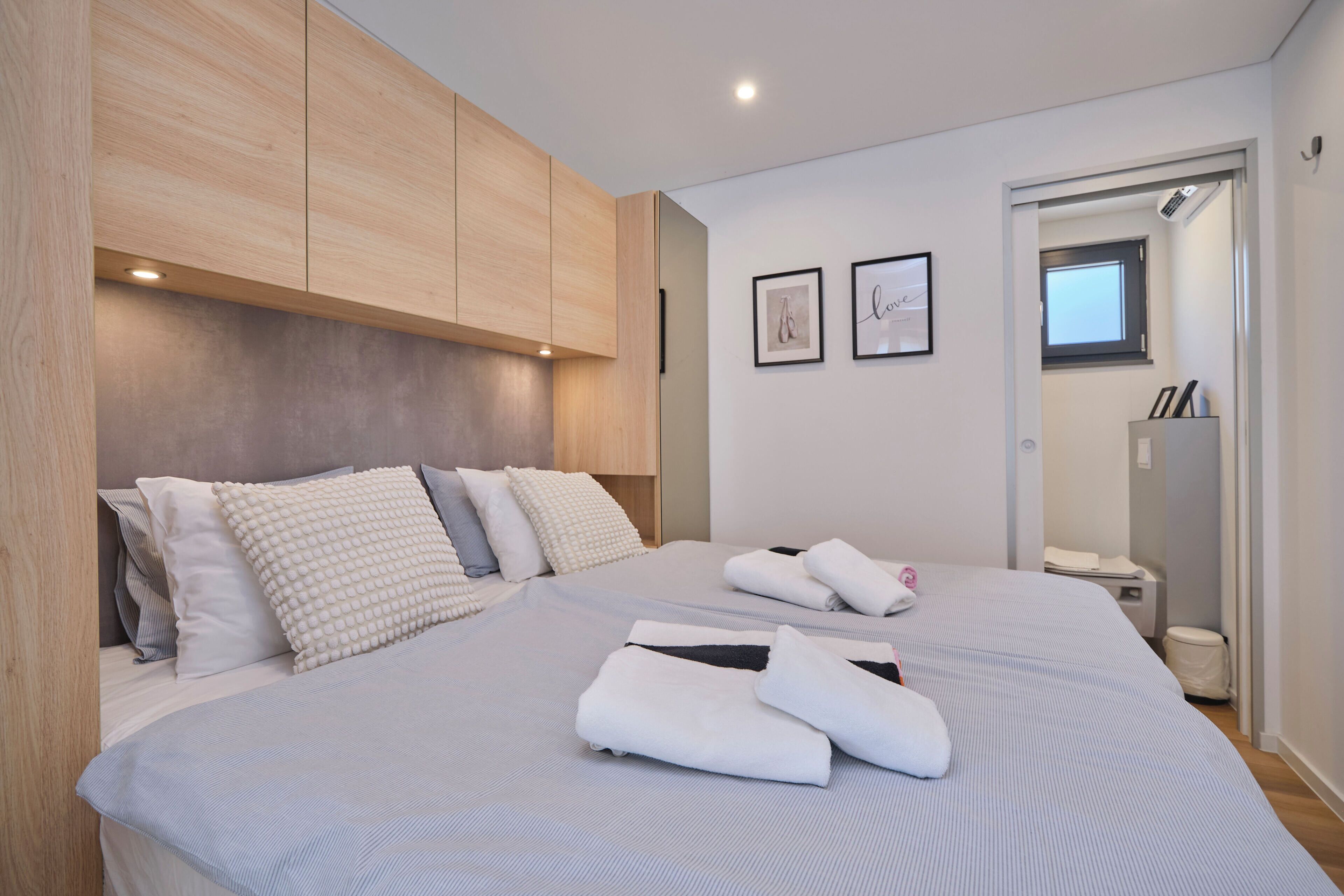 Une chambre à coucher moderne avec un grand lit, une tête de lit en bois et une petite salle de bain visible à travers une porte ouverte.