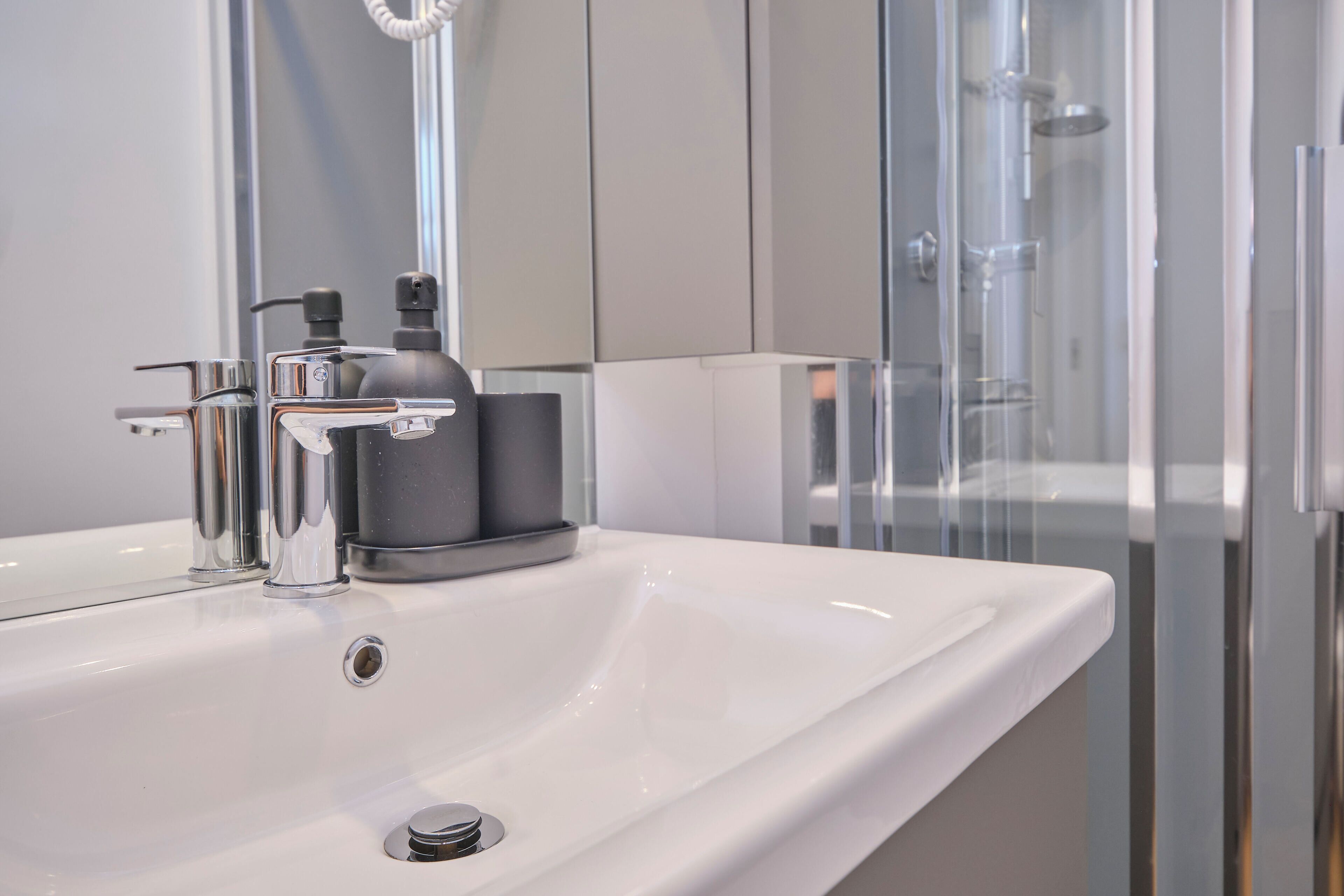 A modern bathroom with a white sink, chrome faucet, and a glass shower enclosure.